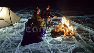 夜间有三个乘火的旅行者在冰上。 在冰上露营。 帐篷就在火旁边。 贝加尔湖。 就在附近